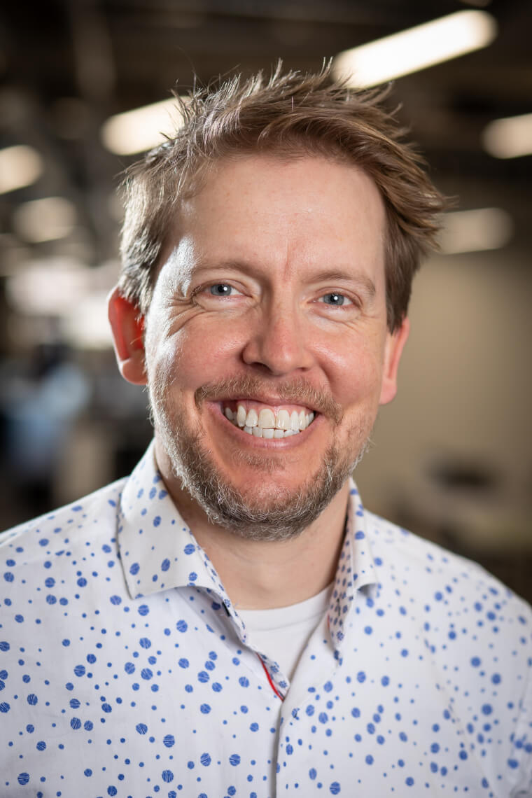 Smiling man wearing a collard shirt with small dots.