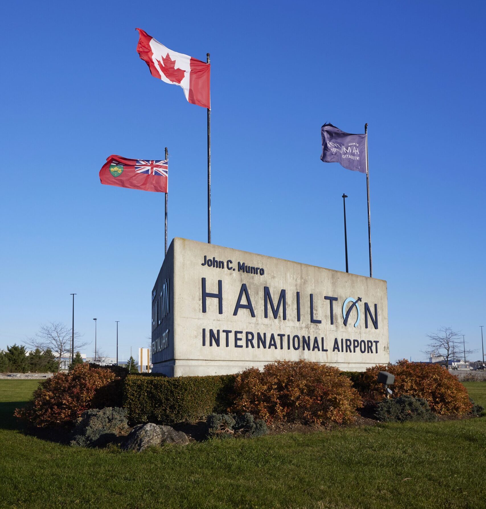 Airport sign with Canadian flag, Ontario flag, and Airport flag. Text: John C. Munro Hamilton International Airport.