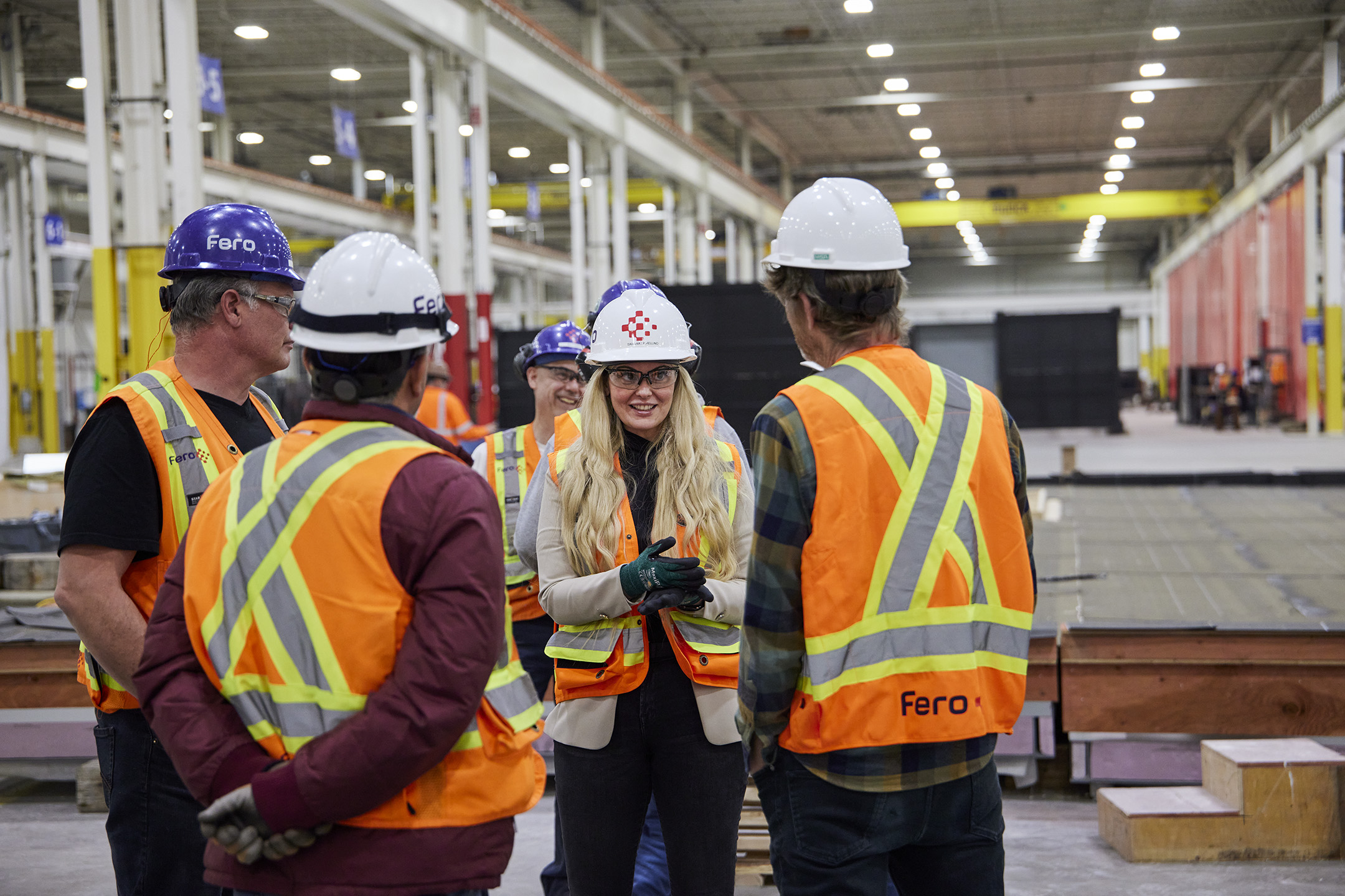 Workers wearing hard hats and safety vests having a huddle in an industrial building.